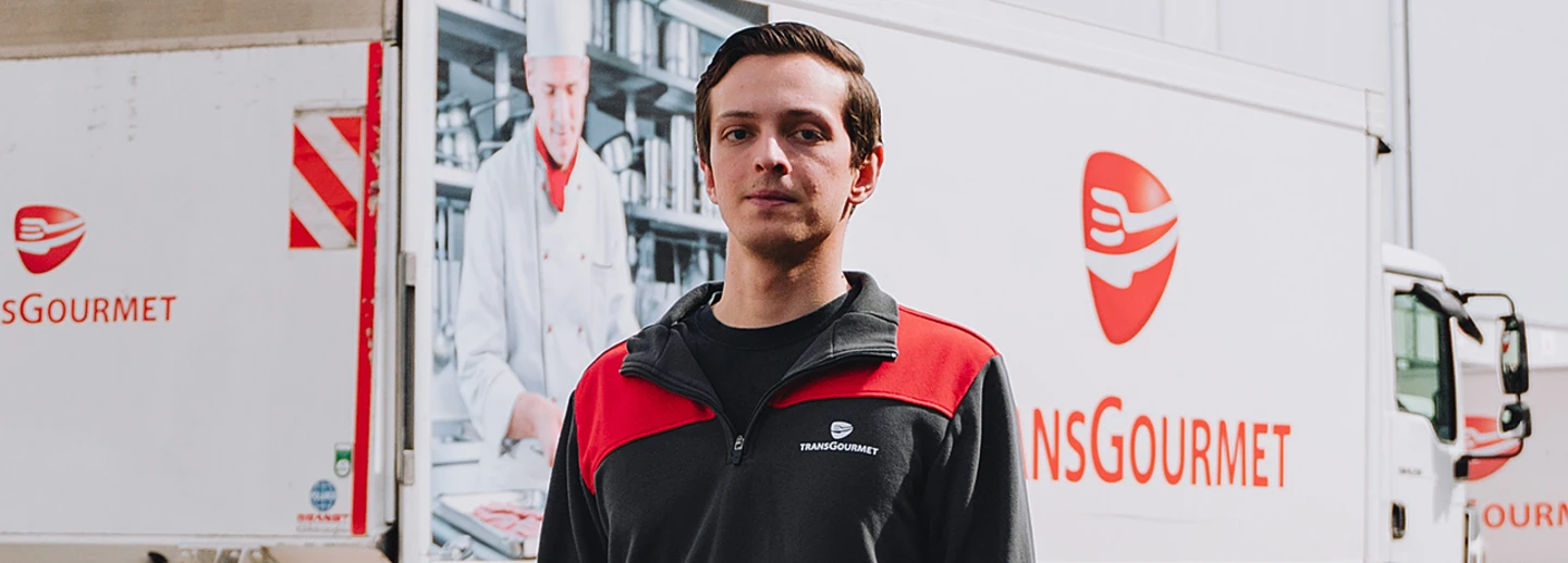 Unser Auszubildender Dimitry steht vor einem Transgourmet LKW auf dem Hof eines Logistikbetriebs von Transgourmet