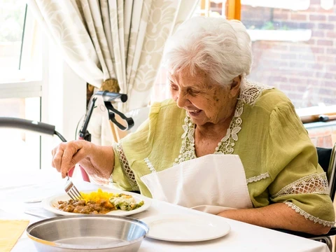 Glückliche Seniorin in einem Rollstuhl beim Mittagessen in einem Seniorenheim
